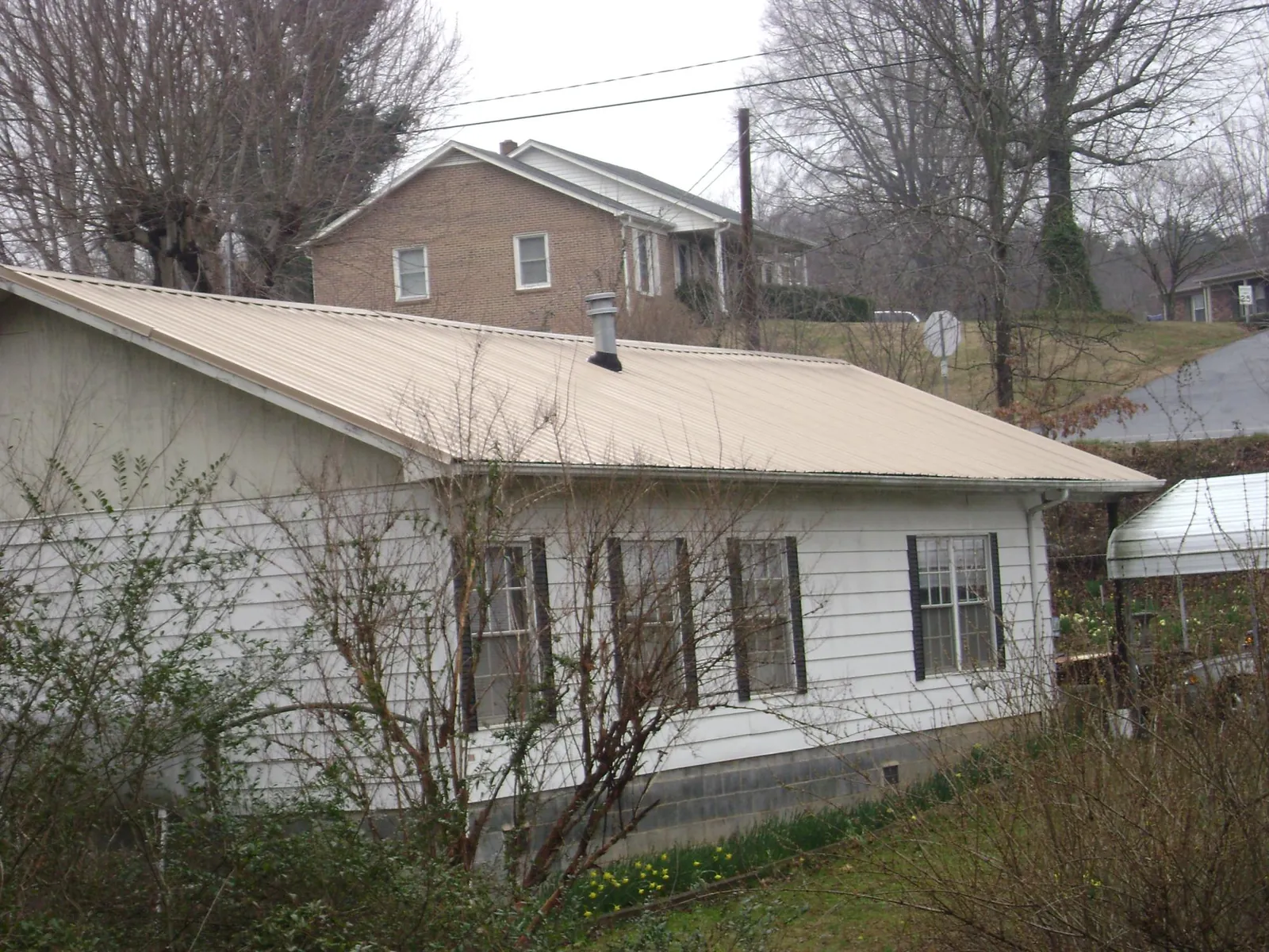 Tan metal roof on a white sided house set into a hillside — Commercial Roofing by Roofing Brothers in Athens